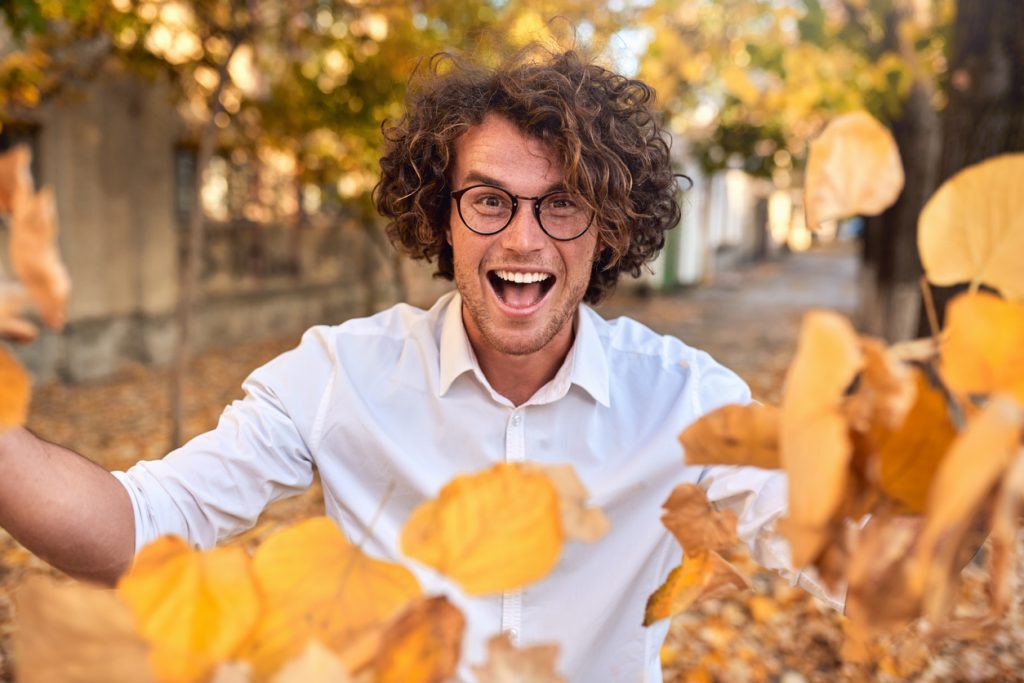 man with glasses smiling while leaves fall
